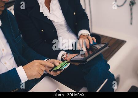 Midsection of senior man holding credit card while woman using digital tablet in yacht Stock Photo