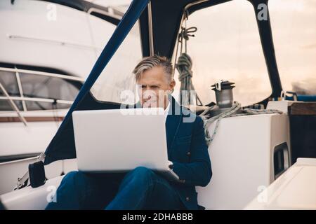 Senior man using laptop while sitting in yacht Stock Photo
