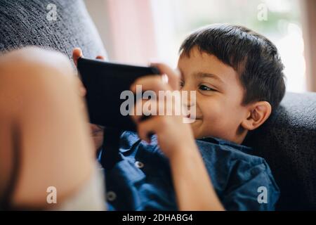 Smiling boy using phone while lying on sofa Stock Photo