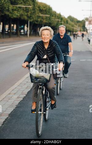 Smiling senior woman with man riding bicycles on city street Stock Photo
