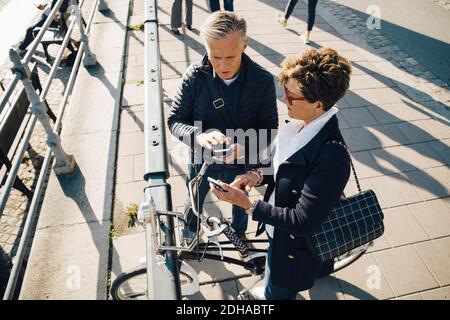 High angle view of senior couple using mobile phones while standing on sidewalk in city Stock Photo