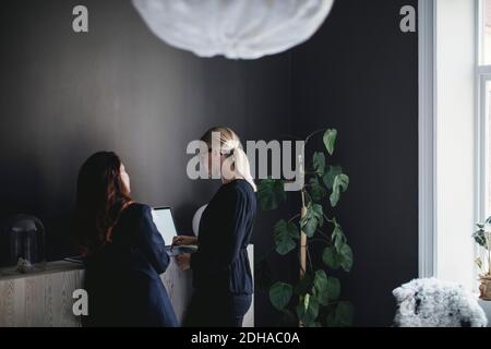 Female coworkers discussing over laptop on cabinet in home office Stock Photo