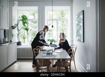 Female colleagues discussing over document at table in home office Stock Photo