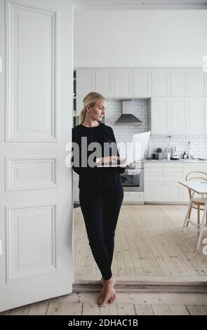 Businesswoman using laptop while standing at doorway in home office Stock Photo