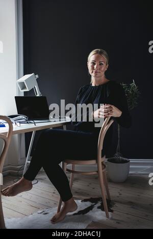 Portrait of businesswoman sitting on chair by desk in home office Stock Photo