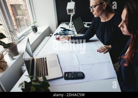 Female engineers discussing over blueprint on desk at home office Stock Photo
