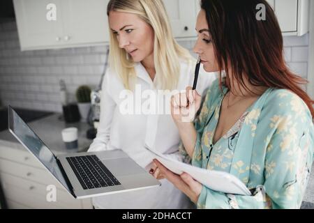 Female colleagues discussing over laptop in kitchen at home Stock Photo