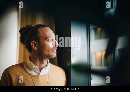 Thoughtful businessman looking through window standing at office Stock Photo