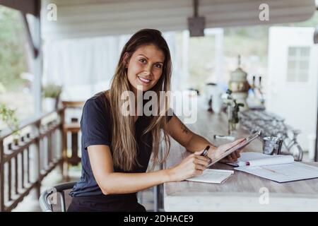 Portrait of smiling female owner using digital tablet while in restaurant Stock Photo