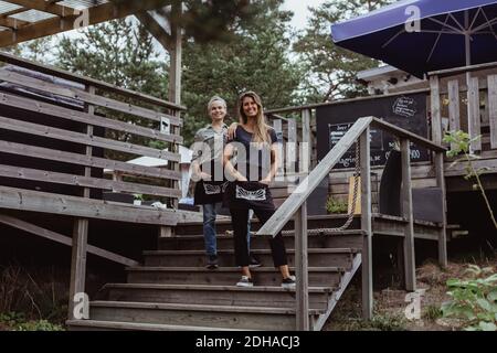 Full length portrait of smiling coworkers standing on steps in restaurant Stock Photo