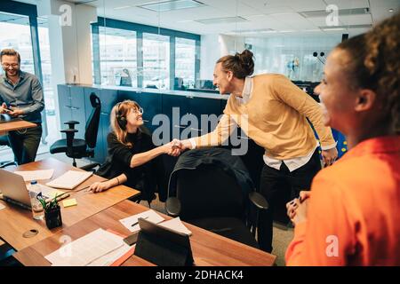 Happy colleagues shaking hands in office Stock Photo