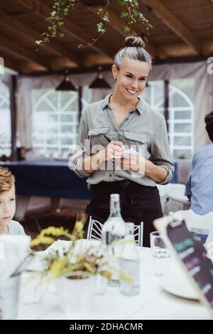 Smiling female owner taking order from customer while standing in restaurant Stock Photo