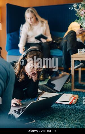 Young businesswoman using laptop while sitting amidst colleagues in cafeteria at office Stock Photo