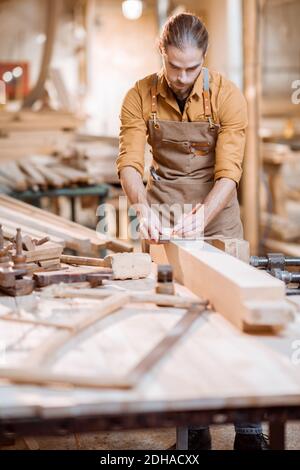 Handsome carpenter working with a wood, marking plank with a pencil in the carpentry workshop Stock Photo