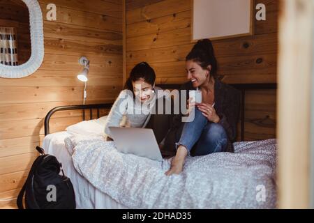 Smiling female friends using laptop while sitting on bed at home Stock Photo