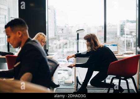 Side view of businessman working against female colleagues discussing over document at office Stock Photo
