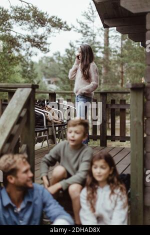 Father sitting with children on steps while woman talking on mobile phone in porch Stock Photo