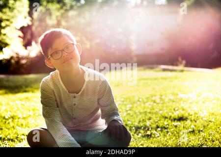 Portrait of disabled boy sitting on grassy field during sunny day Stock Photo