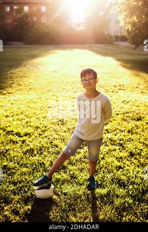 Portrait of smiling boy with soccer ball standing on grassy field at park Stock Photo