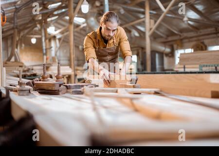 Handsome carpenter working with a wood, planing a bar with a plane in the carpentry workshop Stock Photo