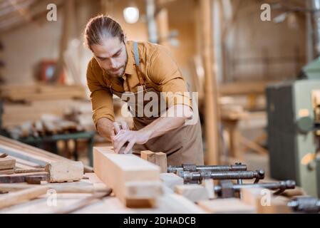 Handsome carpenter working with a wood, planing a bar with a plane in the carpentry workshop Stock Photo