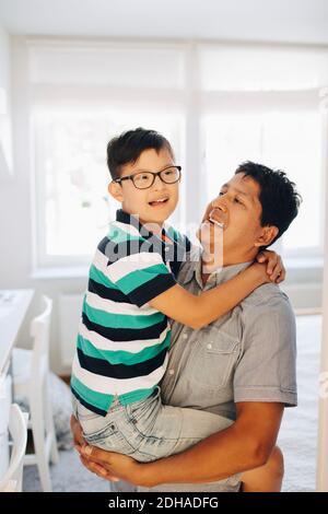 Happy father carrying disabled son while standing at home Stock Photo