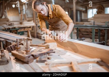 Handsome carpenter working with a wood, planing a bar with a plane in the carpentry workshop Stock Photo