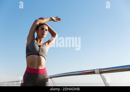 Low angle shot of attractive fit woman in sports bra and leggings, doing stretch exercises before jogging. Girl workout on the s Stock Photo