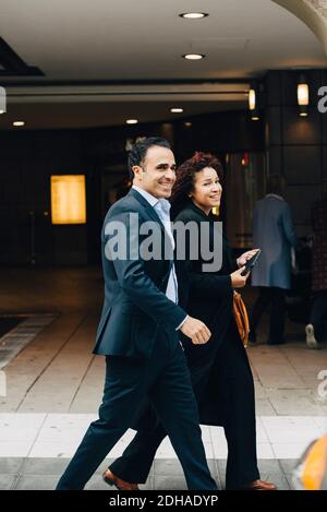 Side view of smiling business colleagues walking on sidewalk in city Stock Photo
