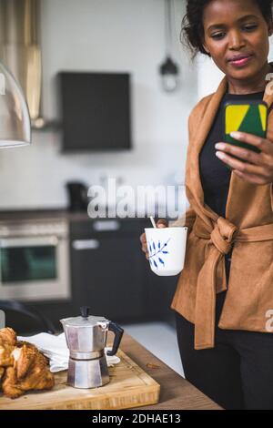 Confident female architect using phone while standing with cup at home Stock Photo