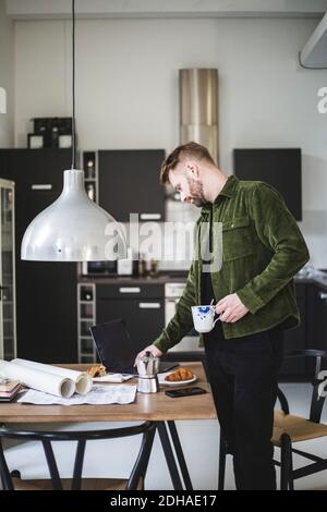 Male architect using laptop while standing with cup by table Stock Photo