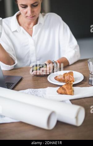 Female freelancer using phone while sitting by table at home Stock Photo