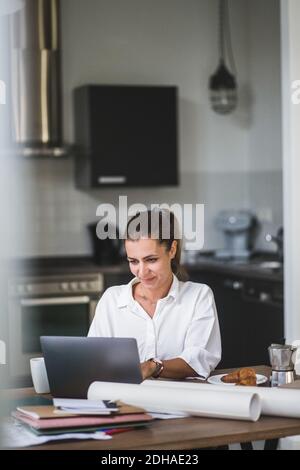 Smiling female freelancer using laptop while sitting by table at home Stock Photo