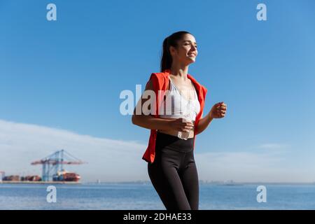 Low angle shot of happy woman running on seaside promenade. Sportswoman jogging in the morning on fresh air Stock Photo