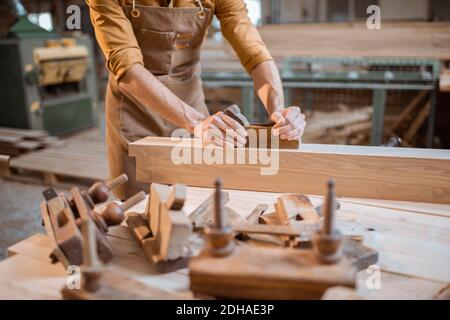 Carpenter working with a wood, planing a bar with a plane in the carpentry workshop. Close-up on hands Stock Photo