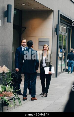 Smiling mature business colleagues talking while standing on footpath by building in city Stock Photo