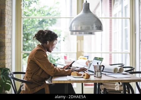 Smiling female architect using phone while sitting at home office Stock Photo