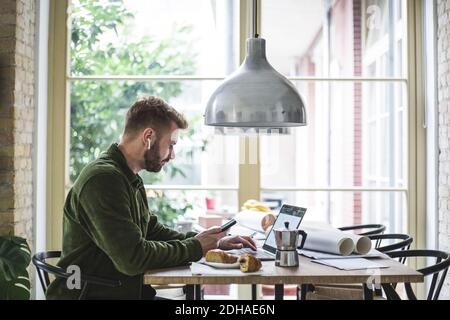 Male entrepreneur using laptop while holding phone at home office Stock Photo