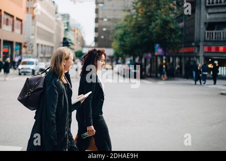 Side view of female business colleagues walking on sidewalk in city Stock Photo