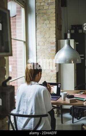 Rear view of female architect talking to coworker through video call while sitting in home office Stock Photo