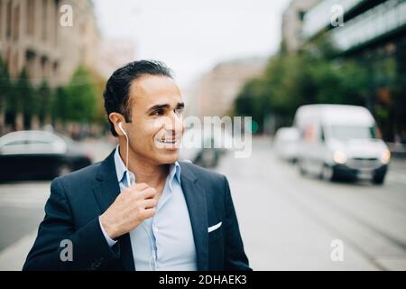 Smiling mature businessman talking through headphones while walking in city Stock Photo