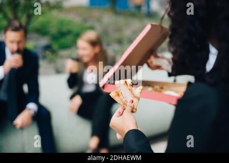 Cropped image of businesswoman holding pizza against colleagues Stock Photo