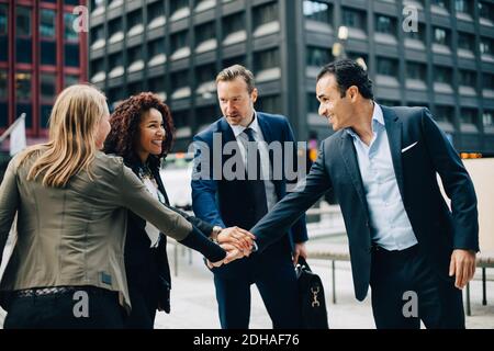 Smiling multi-ethnic business people stacking hands against building in city Stock Photo