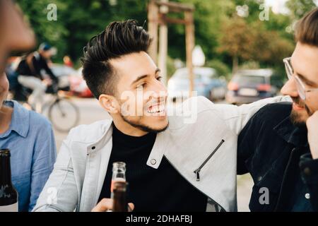 Young man looking at male friend while sitting at garden party Stock Photo