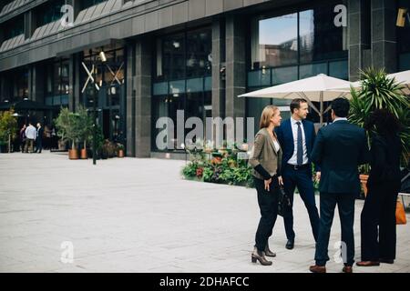 Full length of business colleagues talking while standing on footpath against building Stock Photo