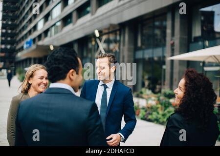 Cheerful business colleagues talking while standing against building in city Stock Photo