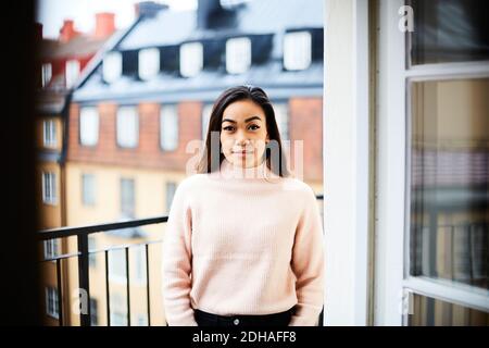 Portrait of smiling young woman standing in balcony seen through door Stock Photo