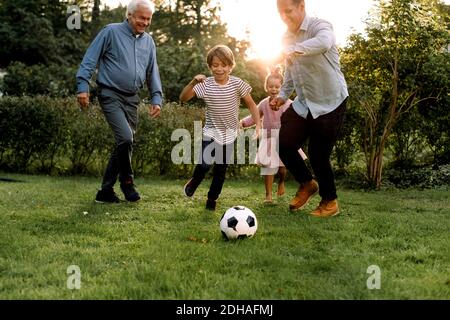 Full length of multi-generation family playing soccer in backyard Stock Photo