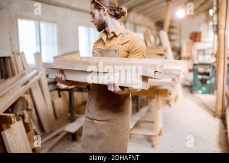 Carpenter carrying pine planks in a carpentry workshop warehouse. Preparing raw materials for the future woodwork Stock Photo