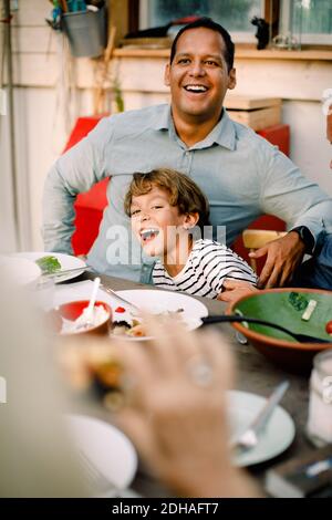 Smiling father and son sitting at dining table during family lunch Stock Photo